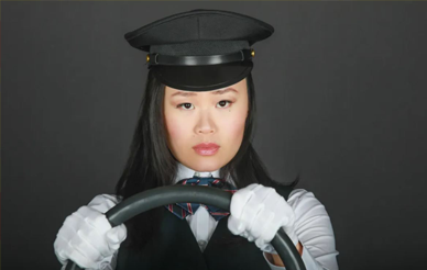 Woman wearing taxi cab driver hat with hands on steering wheel